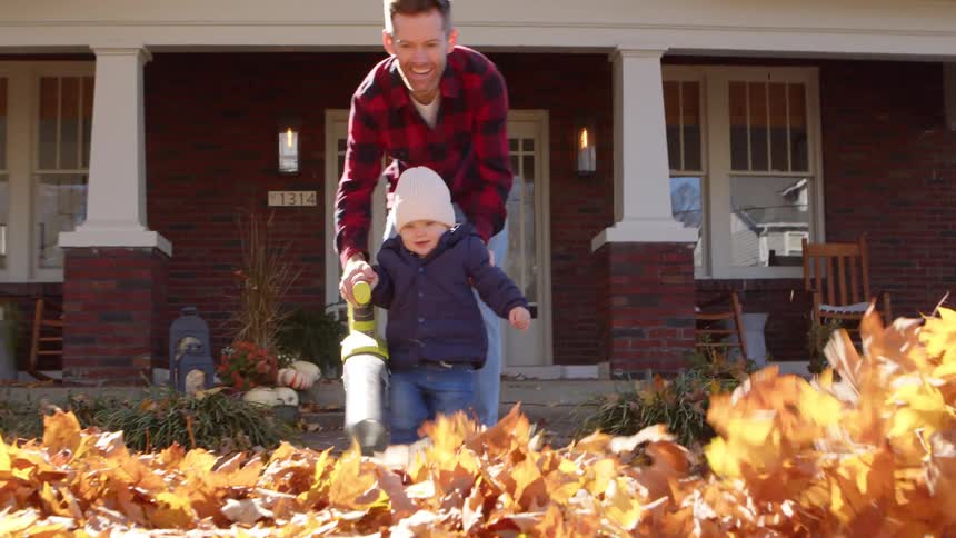 Father with his little son cleaning dry leaves from a yard