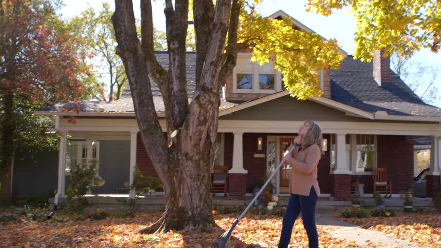 A woman is faking leaves in front of her home