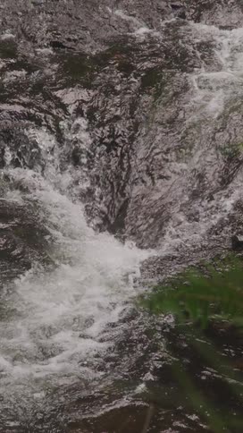A river of water forcefully gushes over rocks into a large dip creating a white crest