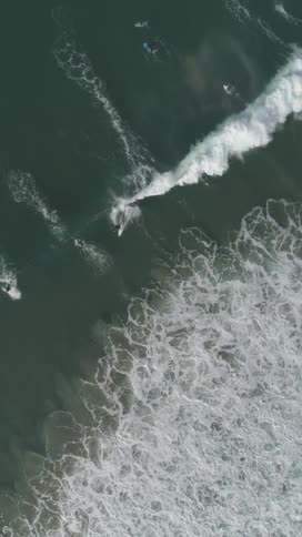 Surfers ride choppy waves in open water surrounded by white foam and turbulent swells