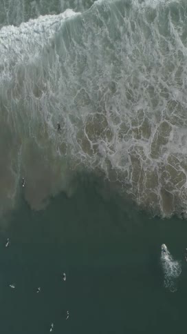 Surfers surf across waves becoming foaming water