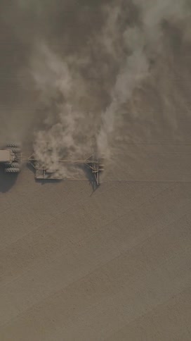 An aerial shot captures a tractor tilling a vast dry brown field leaving a trail of kickedup dust in its wake