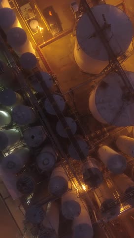A vast industrial plant at night illuminated by orange lights with numerous large storage tanks and complex structures