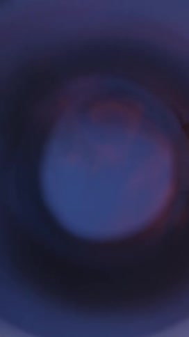 A closeup of flames and smoke from a deflagration contained within a metallic tube set against a blue background
