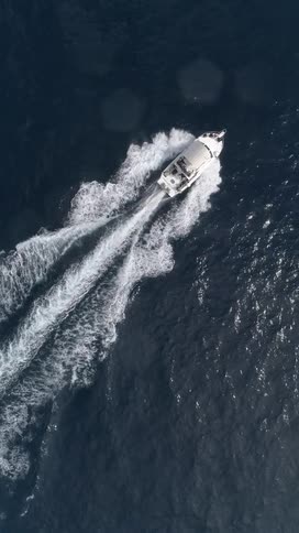 An aerial view of a white boat racing across dark blue water carving a sharp white wake in its path