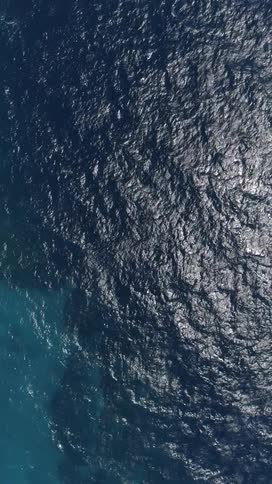 The surface of the ocean is shown with light reflecting off of it via aerial view