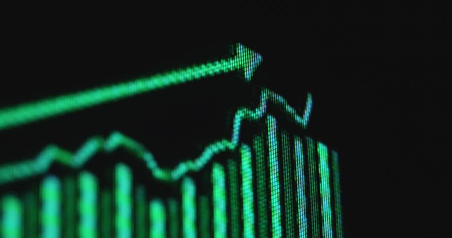 The neon green pixels of a retro tube television screen display a sales chart or graph on a black background moving upwards representing a positive statistic and data for a corporate presentation