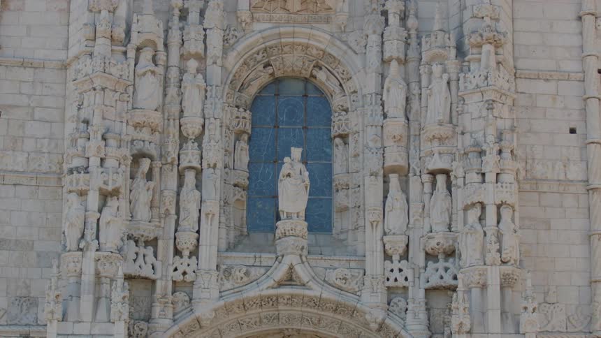 A statue stands in front of a window on a cathedral