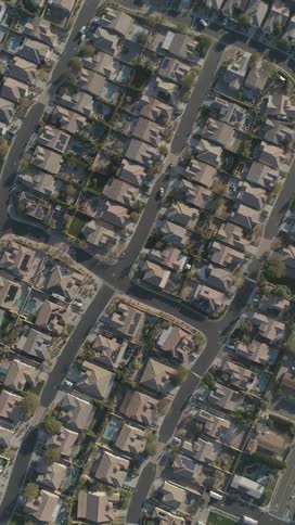 An aerial view shows a residential neighborhood with numerous houses and winding streets under clear daylight
