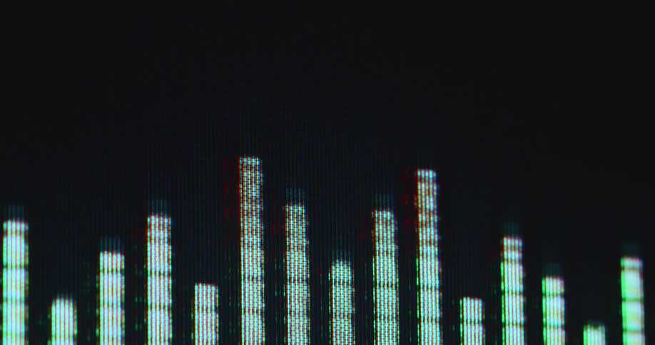 Closeup of digital audio equalizer display shows green pixelated vertical bars fluctuating against a dark background representing sound waves as the loud music causes audio channels to clip with red indicator signal and distortion