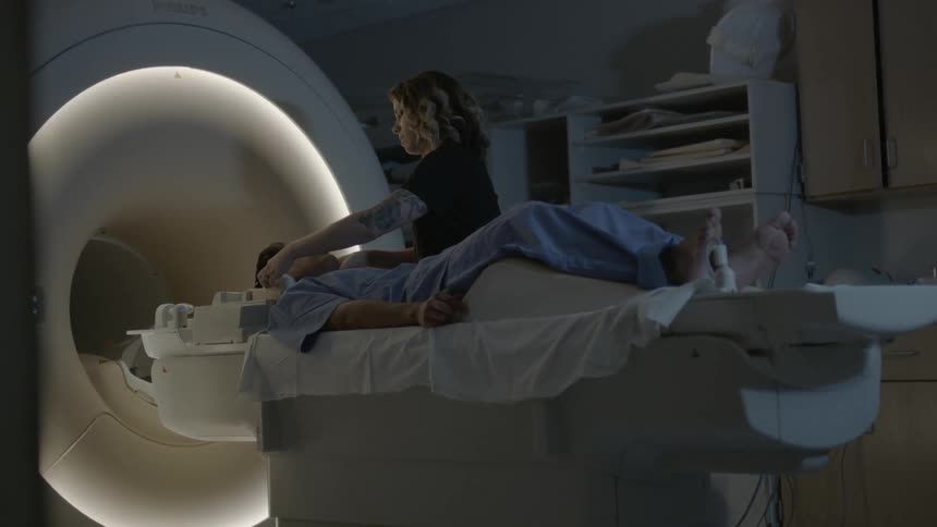 A technician puts earphones on a man about to be placed in an mri machine