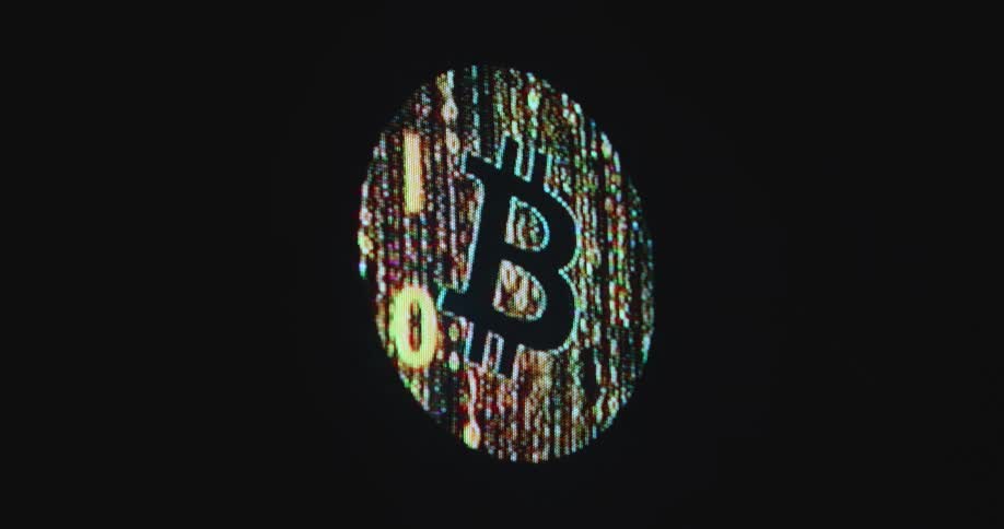 The original Bitcoin or BTC logo created by crypto currency developer Satoshi Nakamoto animated on a computer screen composed of illuminated digital zeros and ones is displayed in front of dark background