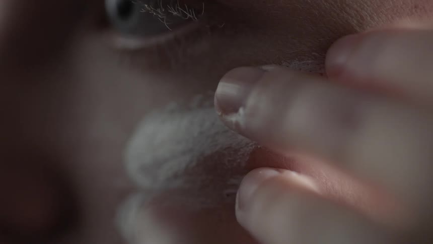 A person rubs a white cream under their eye