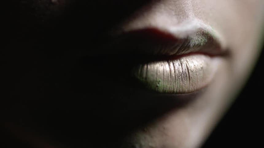 A woman wearing gold lipstick stares towards a light