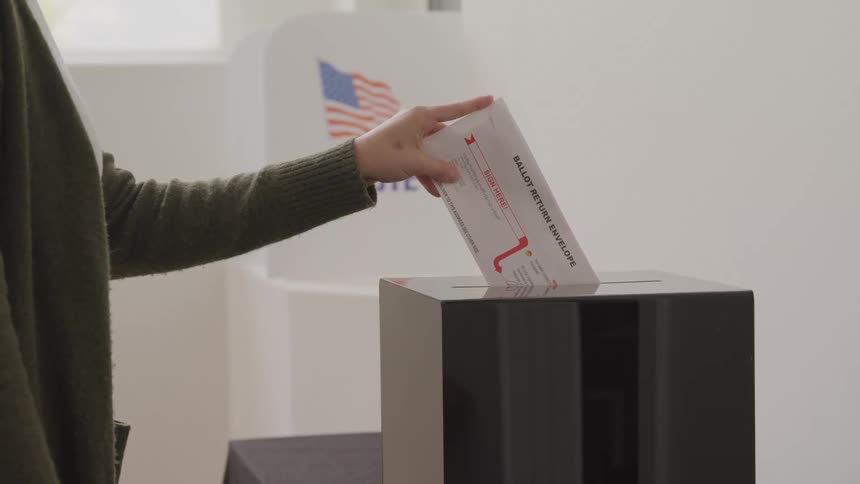 Female voter drops a ballot in the ballot box during the daytime