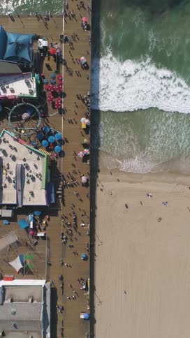 A crowded pier next to a beach with people enjoying the waterfront captured from directly above