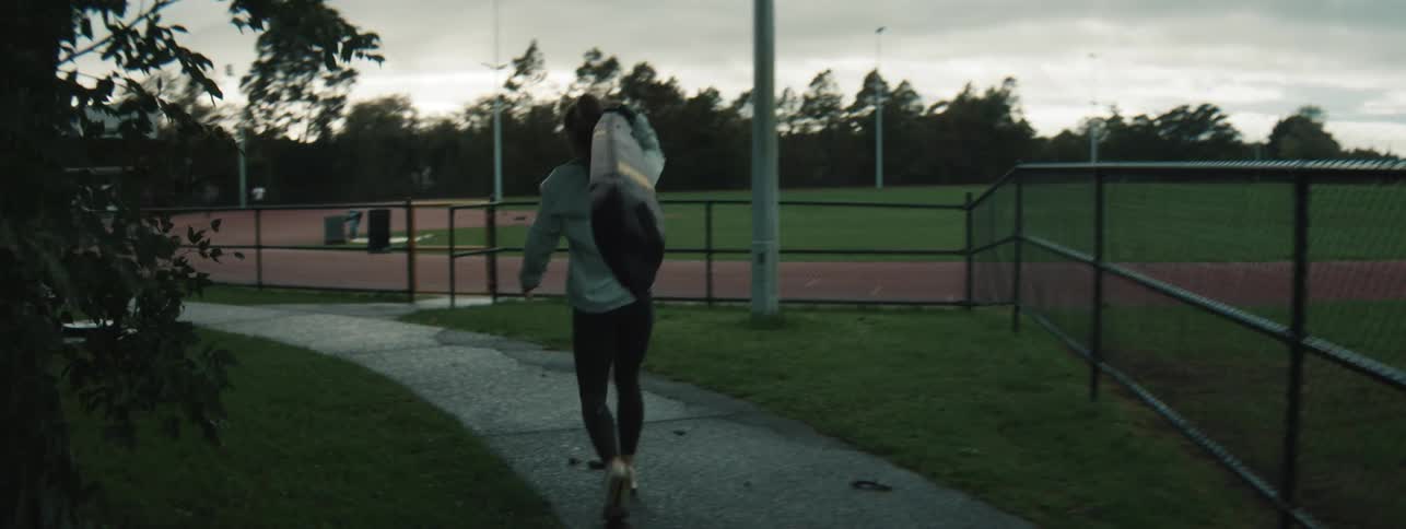 Woman removing sports equipment from a car and walking towards an athletics track
