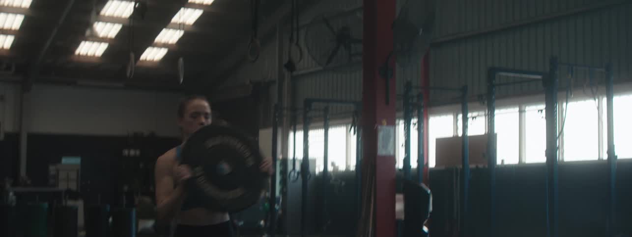Young woman runs and jumps while carrying a gym weight in the air inside a gym