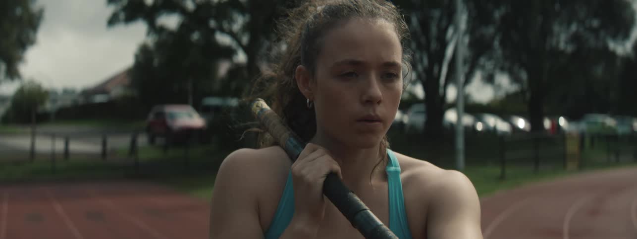 Young female athlete takes a deep breathe while holding a pole in preparation to begin her practice on a track during daytime