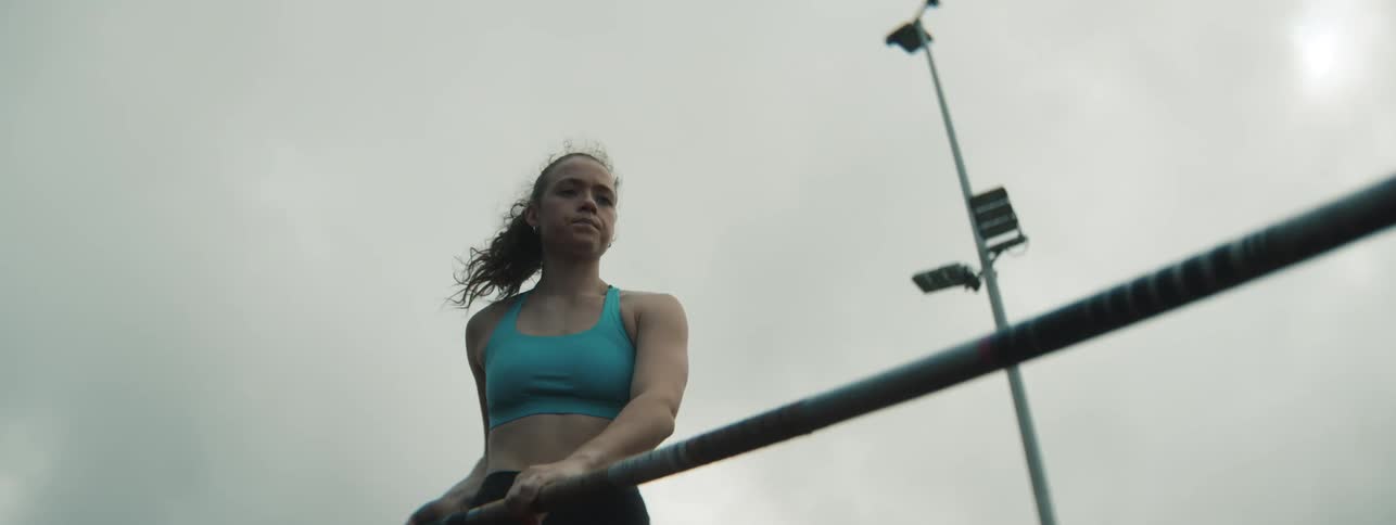 Female athlete inspects and lifts a pole before running on a track outdoors during daytime