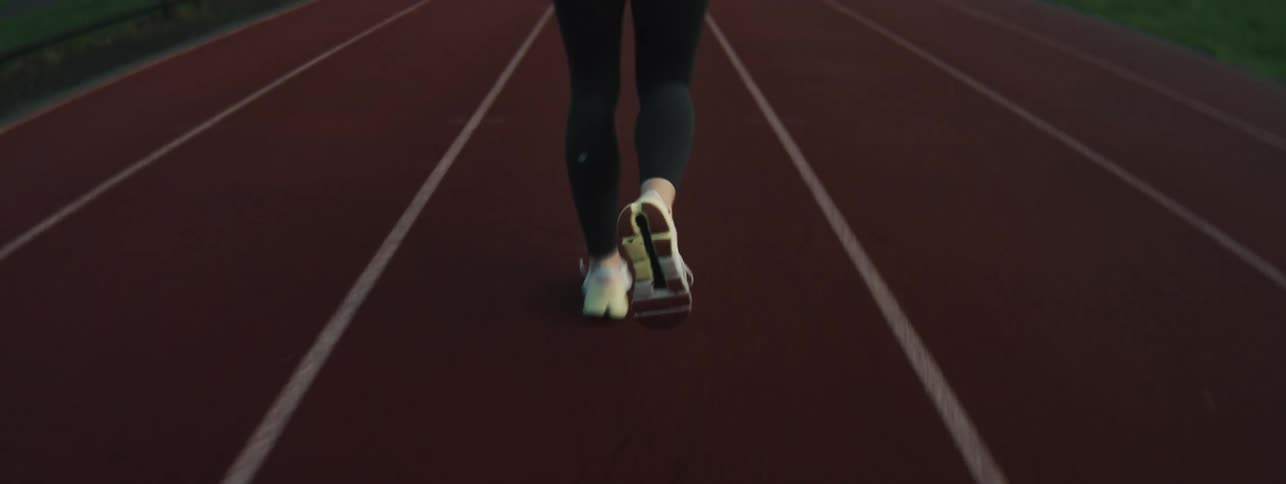 A female athlete wearing sneakers and sportswear runs on a track at midday