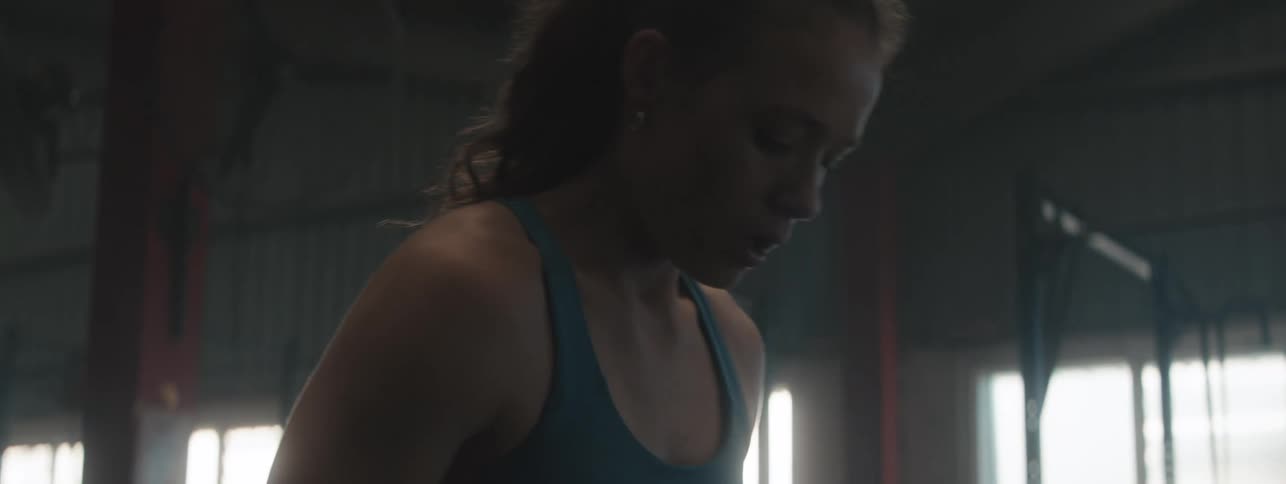 A young woman is performing a deadlift inside a gym framed by racks and weightlifting equipment