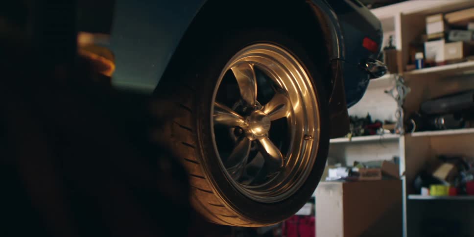 Closeup of a car tire and chrome wheel lifted in a dimly lit garage
