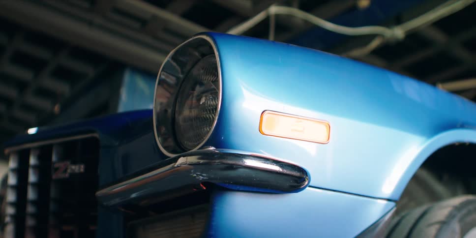 A closeup shot highlights the front corner of a glossy blue vintage car featuring its round headlight chrome bumper and z28 emblem