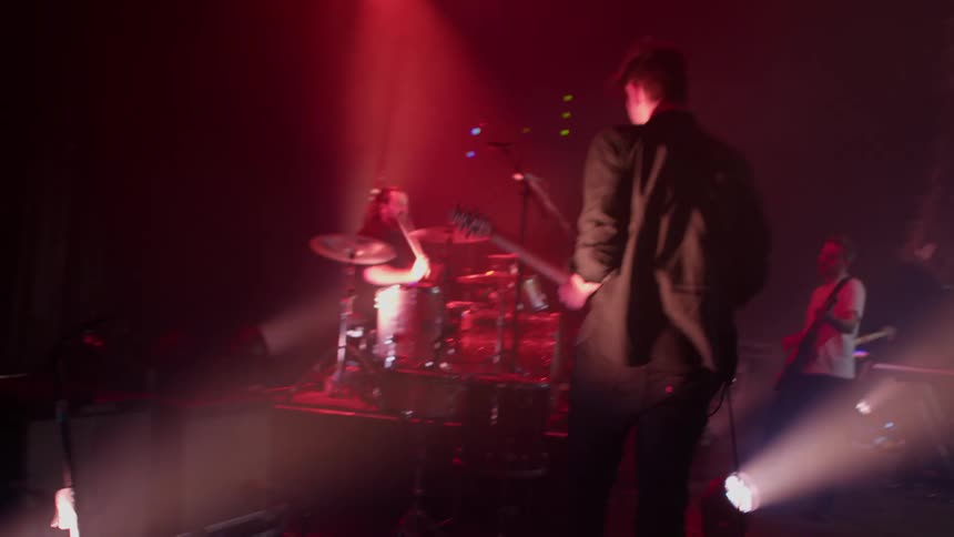 Male guitarist performs on a stage under lights as part of a band at a night concert