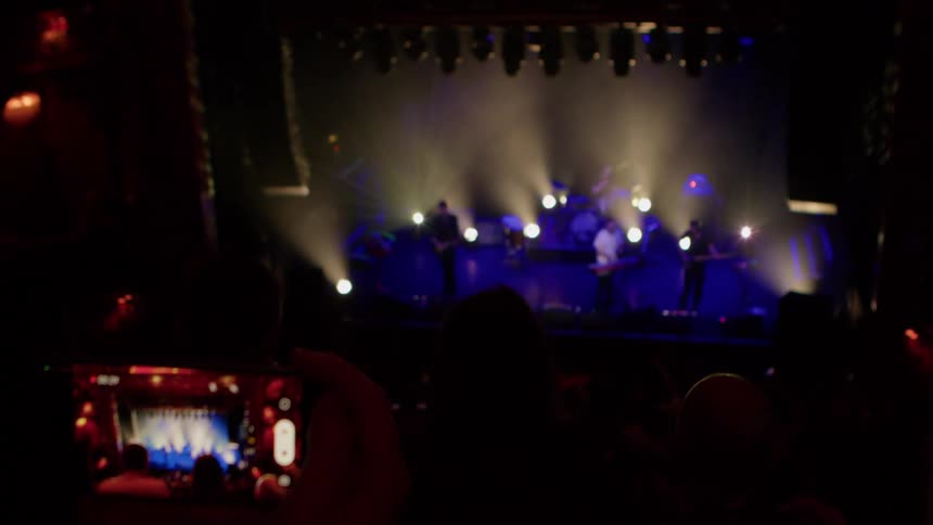 The band is being recording by a member of the crowd with their cell phone