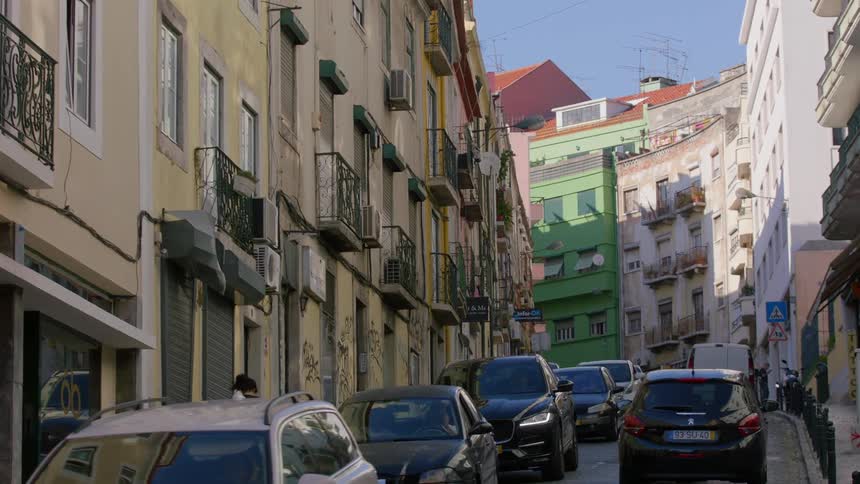 Many vehicles driving down a narrow building lined street