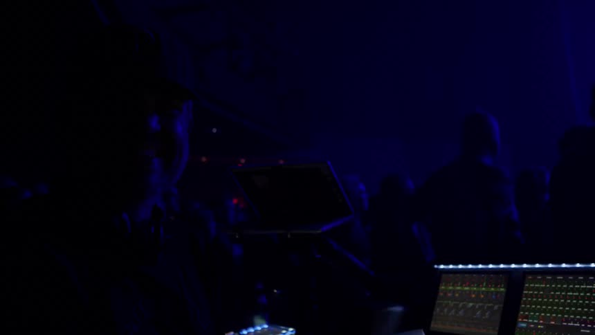 A person operates a sound mixing console in a dimly lit venue during a live performance