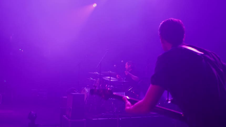 A band performs together on stage under vibrant purple lighting