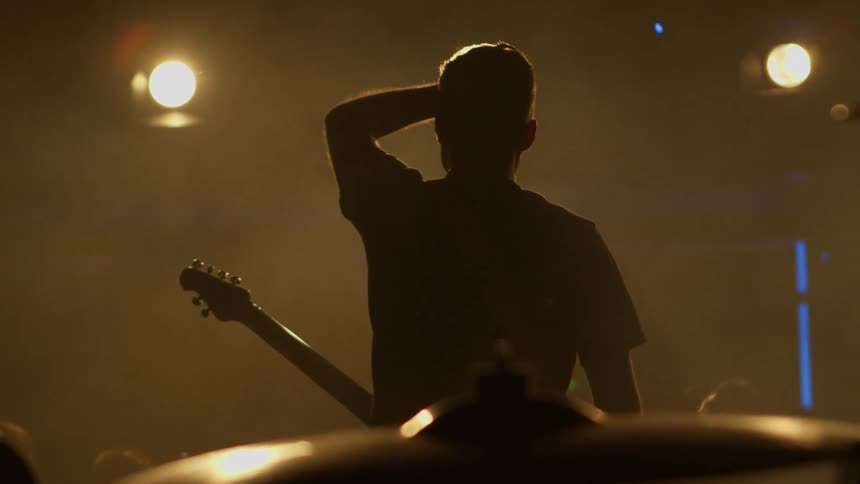 The guitarist is waving at the crowd from the stage
