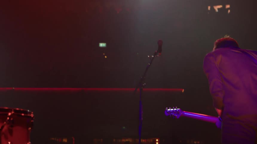 Male guitarist performs on a stage as part of a band at a concert at night