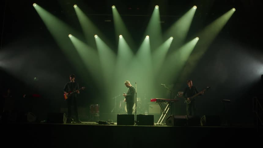 A band performs live on stage under dramatic spotlights in a dark concert venue