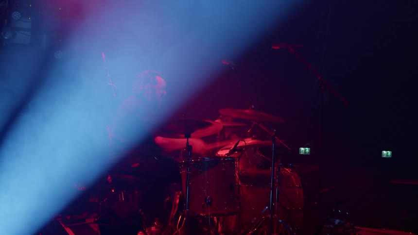A male drummer performs on a stage under stage lights at a concert at night