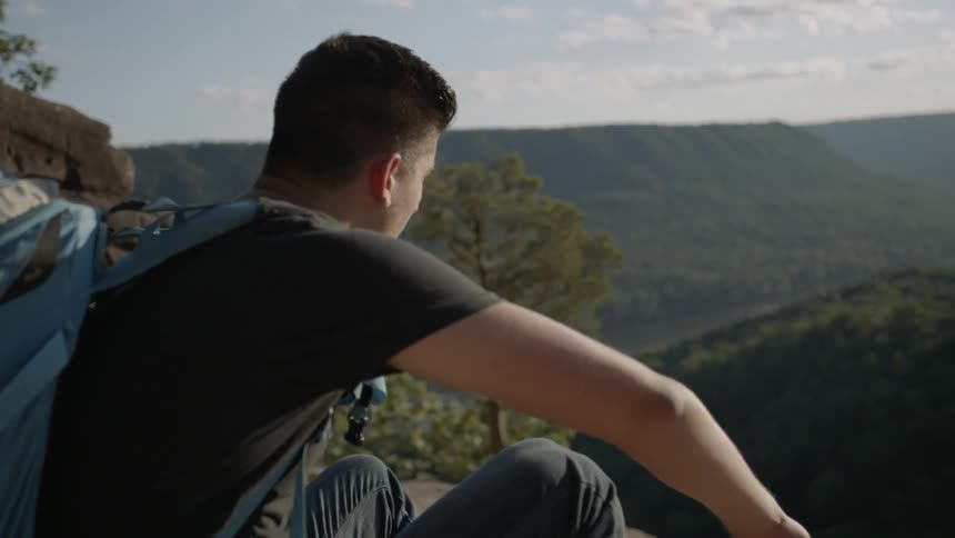 A man crouches down to sit by a cliff