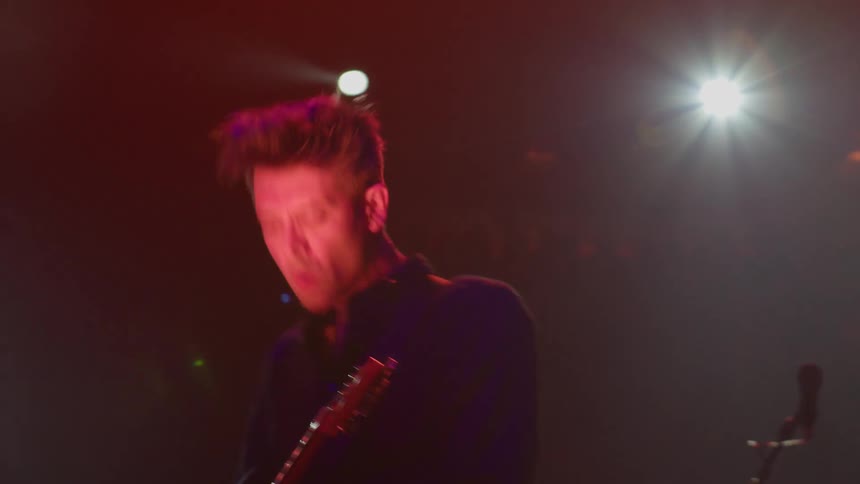 A man wearing a black shirt plays the guitar energetically on stage during a concert