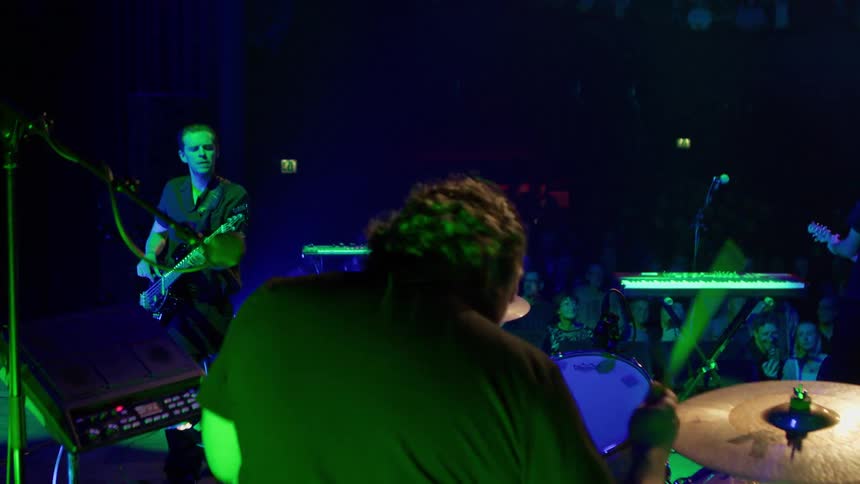 A man playing drums at a rock concert with other musicians beside him playing guitar and bass