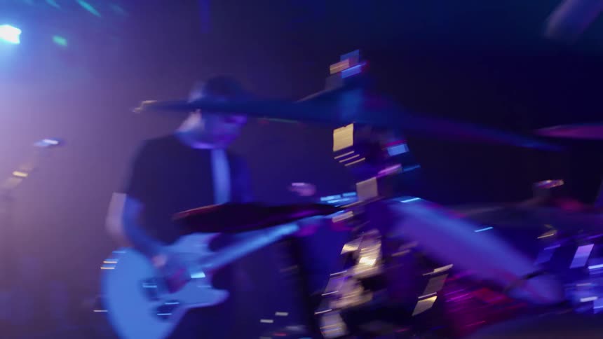 A band performs energetically on stage with a guitarist and drummer driving the rhythm