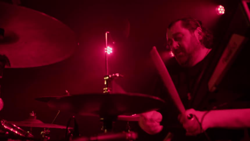 Close up of a male drummer performing on stage under stage lights at a concert at night