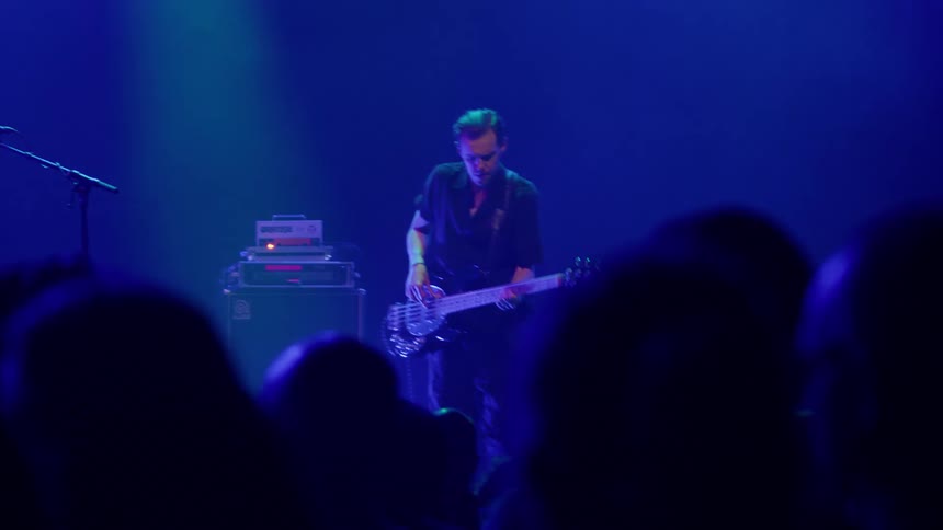 Musician playing bass guitar on stage under blue lighting during a live concert