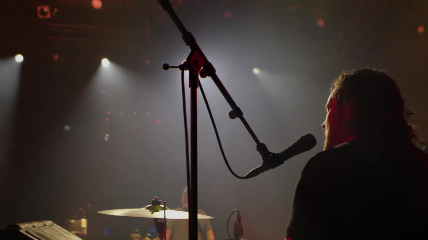An artist performing at a concert playing the drums and singing into a microphone