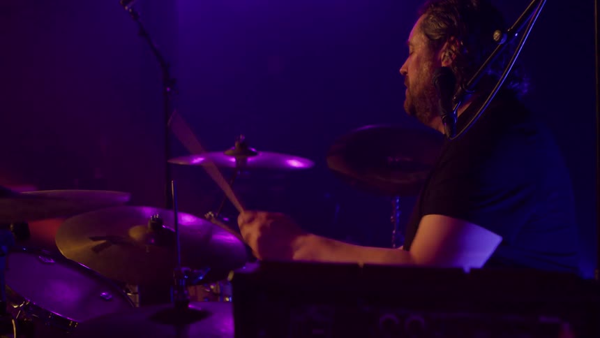 Male drummer performs on stage under stage lights at a concert at night