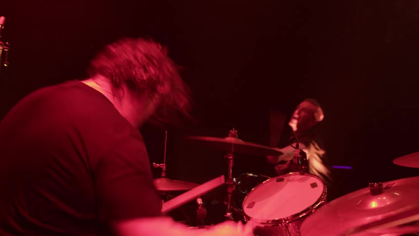 A drummer playing in a rock band with a percussionist performing nearby