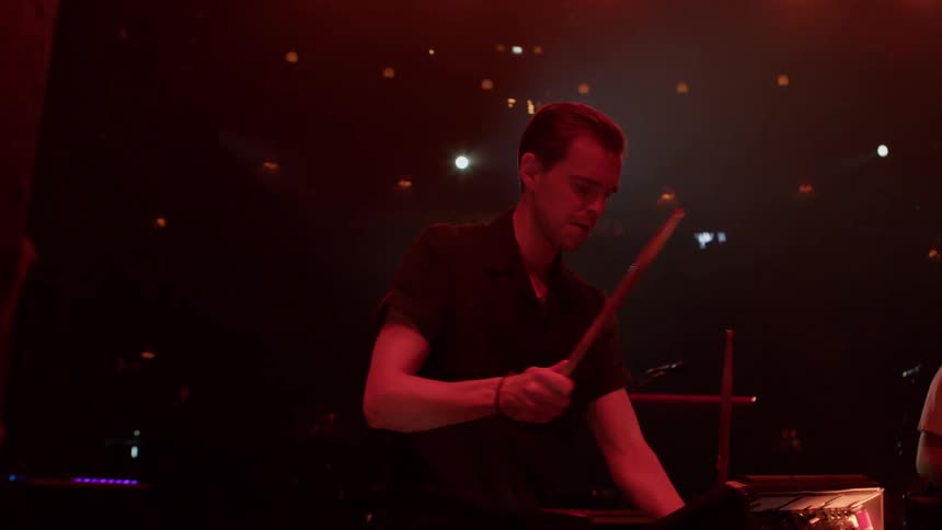Two musicians perform on stage under dramatic lighting one playing drums and the other guitar