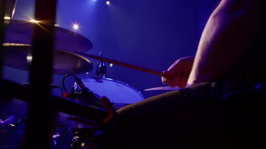 A man passionately plays the drums during a live concert on stage