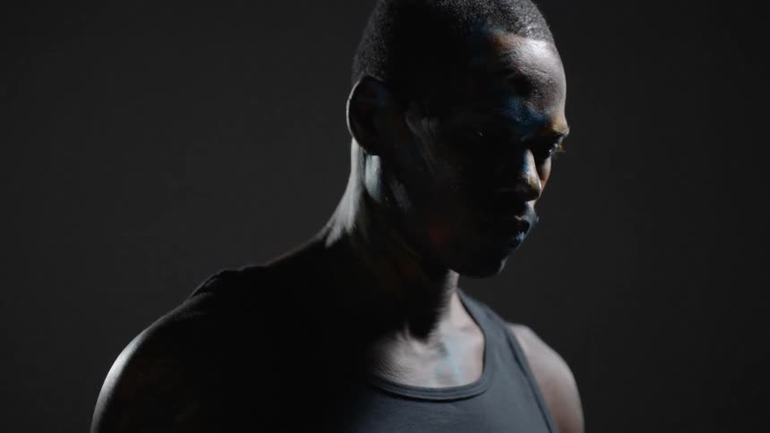 A man with colored chalk on his face turns forward