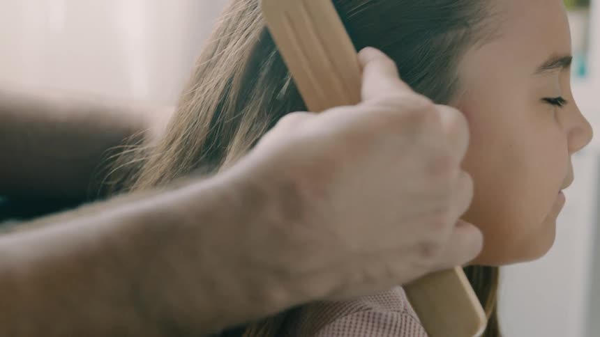A man gently combs his daughters hair as she sits in front of him